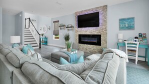 A modern living room with a fireplace, a staircase, and a mounted TV.