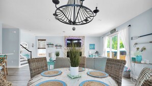 A dining area with a round table, wicker chairs, and a chandelier.
