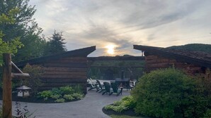 Una cabaña de troncos con un patio, mobiliario exterior y un sendero que lleva a la entrada.