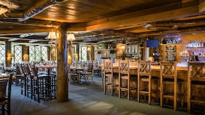 Un interior rústico de madera con mesas y sillas, una zona de bar con botellas y una chimenea de piedra.