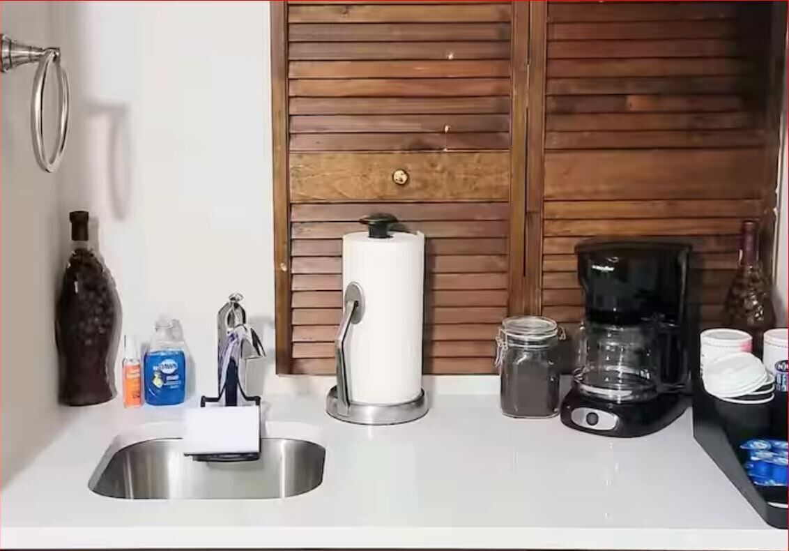 A kitchen with a sink, a coffee maker, a jar, and a bottle.