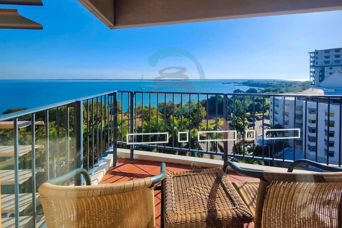 Un balcón con mobiliario de mimbre, vistas despejadas al mar y edificios circundantes.