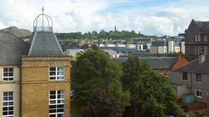 A residential area with brick buildings, a prominent tower with a pointed roof, and a hill with scattered structures in the background. - Stylish 2 Bedroom Apartment Near the City Centre (Edinburgh)