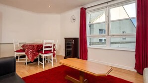 A room with a wooden table, red carpet, white chairs, a clock on the wall, and a window with red curtains. - Stylish 2 Bedroom Apartment Near the City Centre (Edinburgh)