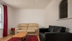 A living room with a beige sofa, a black sofa, a wooden coffee table, and a red rug. - Stylish 2 Bedroom Apartment Near the City Centre (Edinburgh)