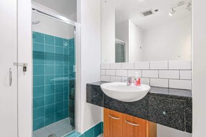 A modern bathroom with a glass shower enclosure, a white sink, and a black countertop.