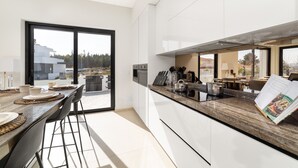 Eine moderne Küche mit einer großen Kochinsel, weißen Schränken und Blick durch die Glastür.