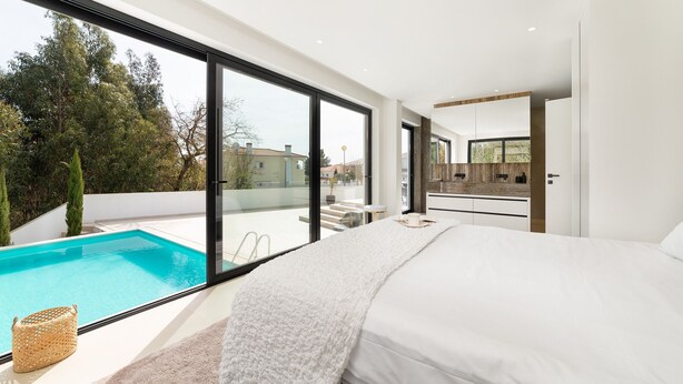 Ein modernes Schlafzimmer mit einem großen Bett, Blick auf einen Swimmingpool und einer Glastür zu einem Außenbereich.