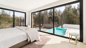 Ein Schlafzimmer mit einem großen Bett, Blick auf einen Swimmingpool und einer Glastür, die nach draußen führt.