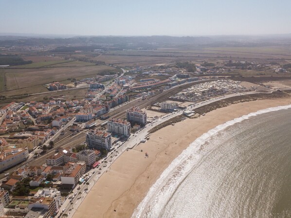 An aerial view of a coastal town with a beach, buildings, and roads.