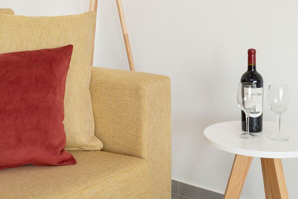 A sofa with a red pillow, a wine bottle, and two glasses on a small white table.