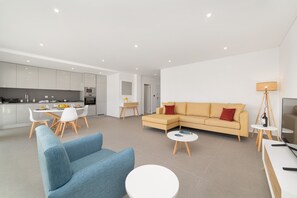 A modern living room with a sofa, a dining table, and a kitchen in the background. - Sunset Views  - T2 Holiday Apartment with sea views By SCH (Nazaré)