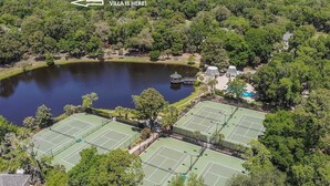 An aerial view of a property with multiple tennis courts, a lake, and a villa marked by an arrow. - Beachfront Resort! Golf & Lagoon View + Pickleball + Easy Beach Access! (Hilton Head Island)