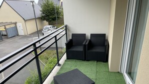 Een balkon met twee zwarte rieten stoelen en een klein zwart voetenbankje op kunstmatig groen gazon.