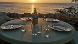 Ein Tisch für zwei Personen, gedeckt mit Riedel-Weingläsern, Gläsern und Tellern, mit Blick auf das Meer bei Sonnenuntergang.