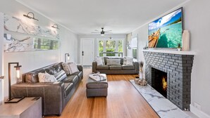 A modern living room with a fireplace, a large TV, and a cozy seating area. - Historic Waterfront 3/2 With Yard & Soaking Tub (Lake Worth)