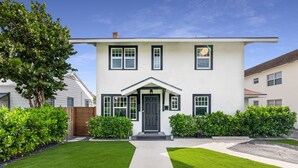 A two-story house with a front entrance, a well-maintained lawn, and a pathway leading to the door. - Historic Waterfront 3/2 With Yard & Soaking Tub (Lake Worth)