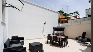 An outdoor patio with wicker furniture, a table with a striped tablecloth, and a swing seat. - Grandma Cecilia's terrace (Lecce)
