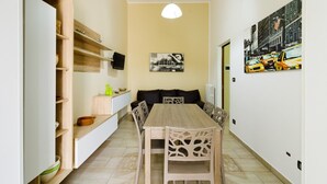 A narrow hallway with a dining area featuring a wooden table and chairs, a black sofa, and a television on a shelf. - Grandma Cecilia's terrace (Lecce)