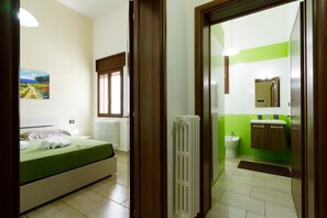 Un dormitorio con cama, radiador y ventana. La habitación tiene una pared verde y un cuadro.