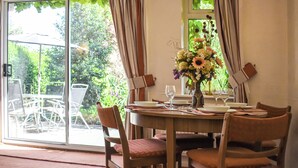 A dining area with a table set for four, chairs, a vase of flowers, and a view through a glass door. - 1 bedroom accommodation in Pickering (Pickering)