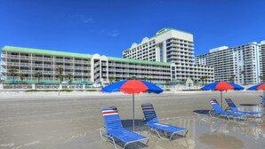 A beachfront hotel with multiple balconies, beach umbrellas, and sun loungers.