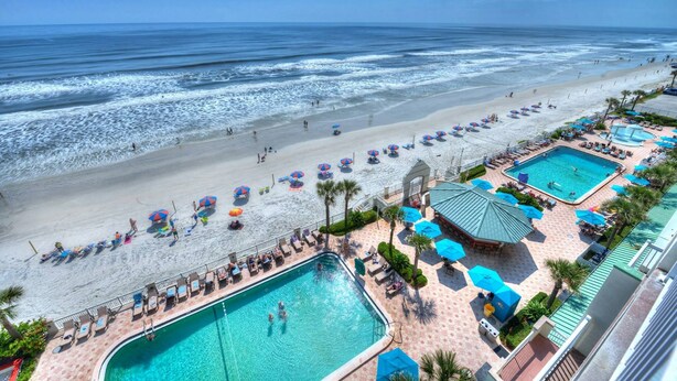 A resort with a large pool, beach area, and multiple umbrellas.