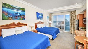 A hotel room with two beds, a balcony with a city view, a dining area, and artwork on the walls.