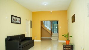 A spacious living room with a black leather sofa, a small wooden table with a potted plant, and a staircase leading to another level. - Incognito Vacation Stay (Kingston)