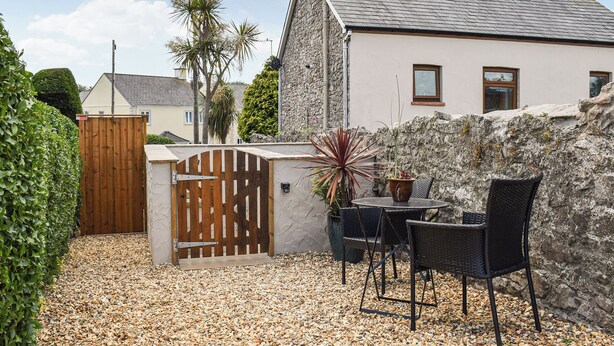 A stone house with a tiled roof, a wooden gate, and a gravel patio with outdoor furniture. - 1 bedroom accommodation in Porthcawl (Porthcawl)