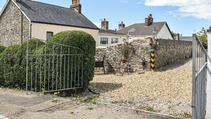 A stone house with a grey roof, a metal gate, and a gravel driveway. - 1 bedroom accommodation in Porthcawl (Porthcawl)