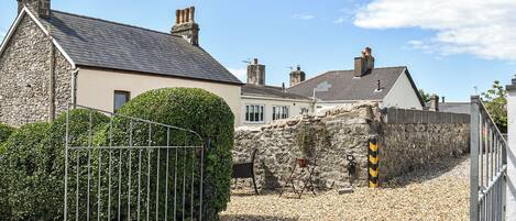 A stone house with a grey roof, a metal gate, and a gravel driveway.