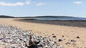 A beach with a rocky foreground and a calm sea in the background. - 1 bedroom accommodation in Porthcawl (Porthcawl)