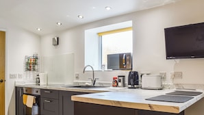 A modern kitchen with a central island, built-in oven, and a flat-screen TV mounted above the island. - 1 bedroom accommodation in Porthcawl (Porthcawl)