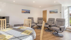 A modern room with a bed, two grey armchairs, a wooden chair, a TV, and two paintings on the wall.