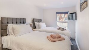 A hotel room with two beds, a TV mounted on the wall, and a window with a view of buildings.