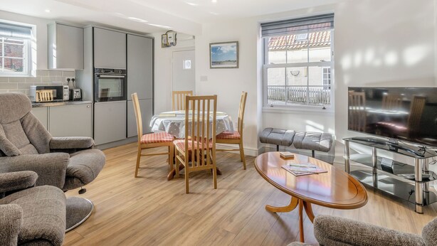 A modern living room with a dining area, kitchen, and a TV.