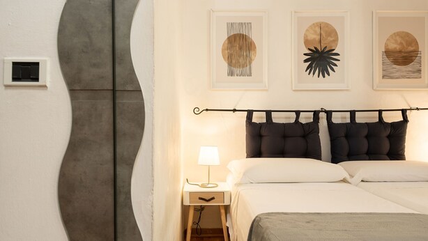 Une chambre à coucher avec un lit, une table de chevet, une lampe et une œuvre d’art abstraite au mur.