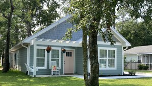 A single-story house with a front porch, a small garden, and a tree in front. - Built in 2021, Cute cottage short walk to beach (Oak Island)