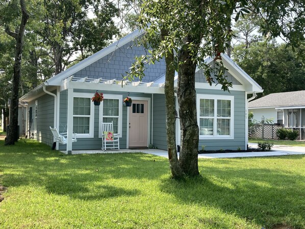 A single-story house with a front porch, a small garden, and a tree in front. - Built in 2021, Cute cottage short walk to beach (Oak Island)