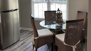 A kitchen with a stainless steel refrigerator, a dining table with wicker chairs, and a chandelier. - Built in 2021, Cute cottage short walk to beach (Oak Island)