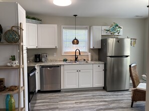 Une cuisine moderne avec des meubles blancs, des appareils en acier inoxydable, un lave-vaisselle intégré et une fenêtre avec des stores.