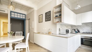 A modern kitchen with white cabinetry, a marble backsplash, and a central island. There is a dining table with chairs and a vase of flowers.