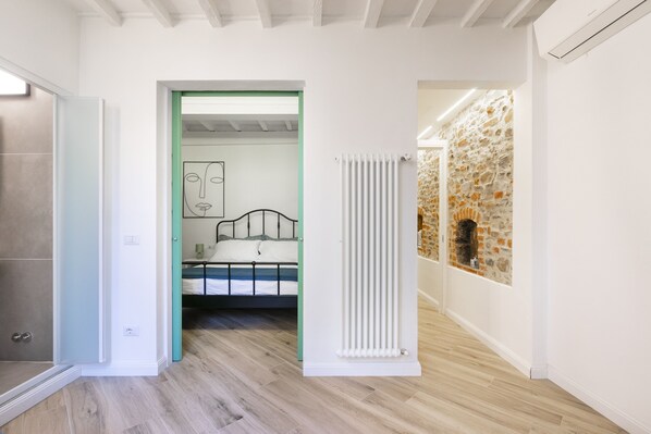 A modern interior with a bed, a radiator, and a stone wall.