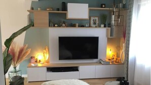 A modern living room with a flat-screen TV, wooden shelves, a white sofa, and a round coffee table. - Pleasant new house Angers Centre-Madeleine (Angers)