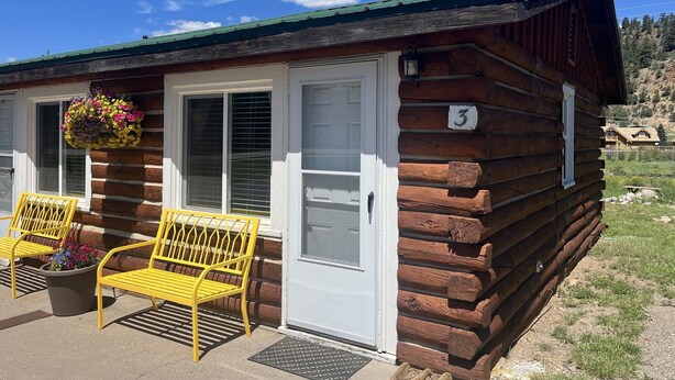 A log cabin with a number '3' on the door, two yellow chairs outside, and a flower basket on the window sill. - Cozy cabin #3 in mountains near Rio Grande River (South Fork)