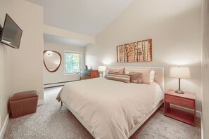 Ein Schlafzimmer mit einem großen Bett, Nachttischen, einem Fernseher, einem Fenster und einem Gemälde an der Wand.