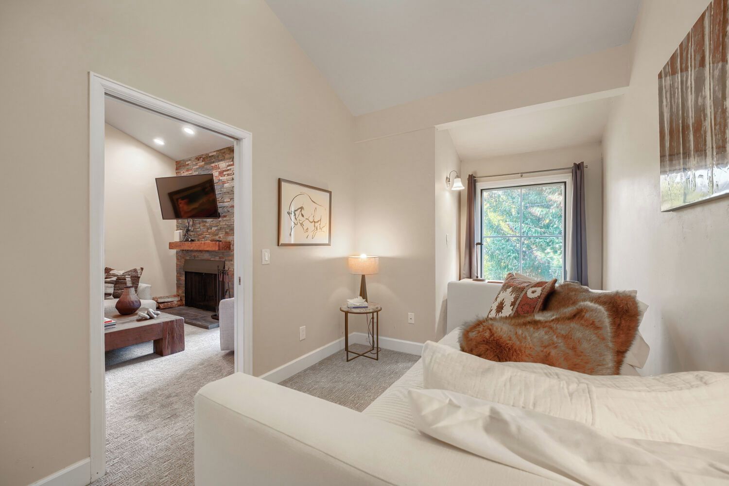 Une chambre à coucher avec un lit, une cheminée, une fenêtre et une porte donnant sur une autre pièce.