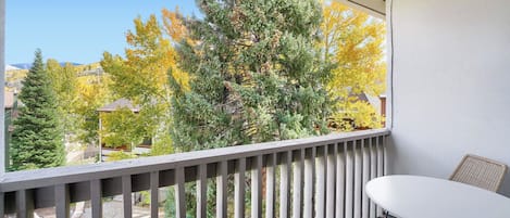 A balcony with a view of trees in autumn colors, a pool, and a table with chairs.