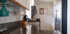 Cozinha com bancadas de granito, geladeira de aço inoxidável e teto de madeira.